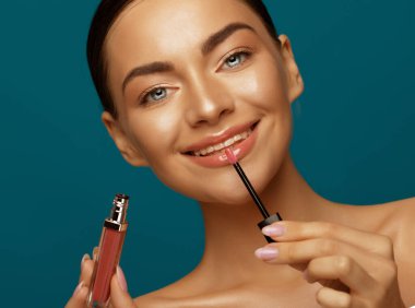 Güzel bir kadın yüzünün yanında ruj tutar, makyaj yapar, makyaj ve makyaj malzemesi konsepti. Mavi arkaplan üzerindeki portreyi kapat,