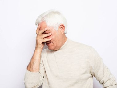 Tatmin olmamış yaşlı bir adam yüzünü eliyle kapatıyor, olumsuz duygular yaşıyor, hayal kırıklığı yaşıyor. Kapat..