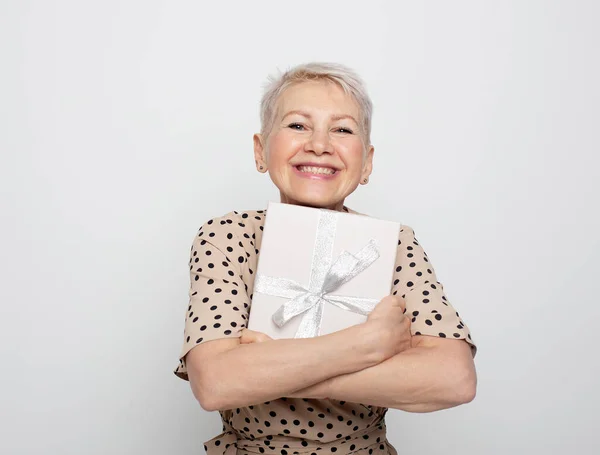 笑着的退休妇女拿着礼物盒的照片 孤立的灰色背景 — 图库照片