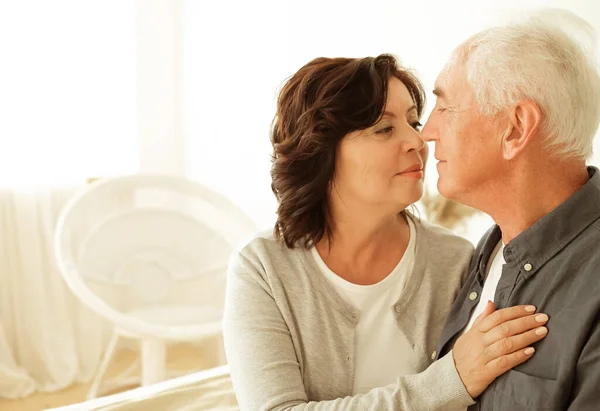 Mature 60 year old couple hugging while sitting on the bed in the bedroom. Lifestyle concept.