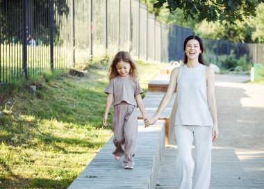 Küçük bir kız annesinin elini tutuyor. Anne ve kızı parkta yürüyor. Yaz zamanı.,