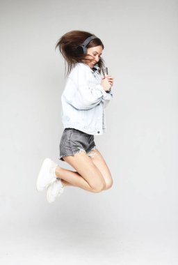 Mikrofonlu mutlu kadın zıplıyor ve gri arka planda şarkı söylüyor.