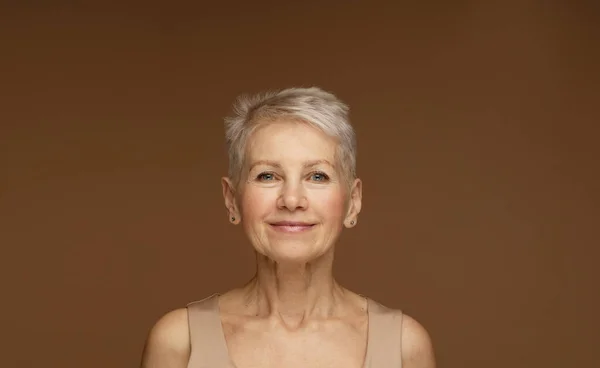 Beautiful elderly woman with a short pixie haircut. Close-up portrait on a brown background.