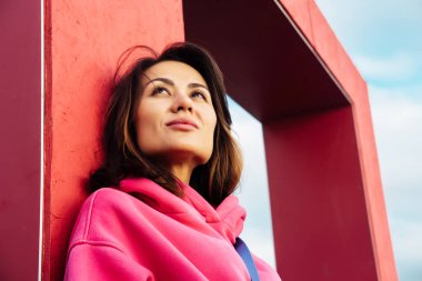 Pembe kazaklı, şık Asyalı genç bir kadın, açık hava portresi.