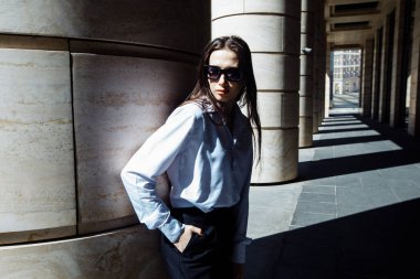 Sokakta poz veren uzun saçlı ve güneş gözlüklü kendine güvenen güzel bir kadının açık hava portresi..