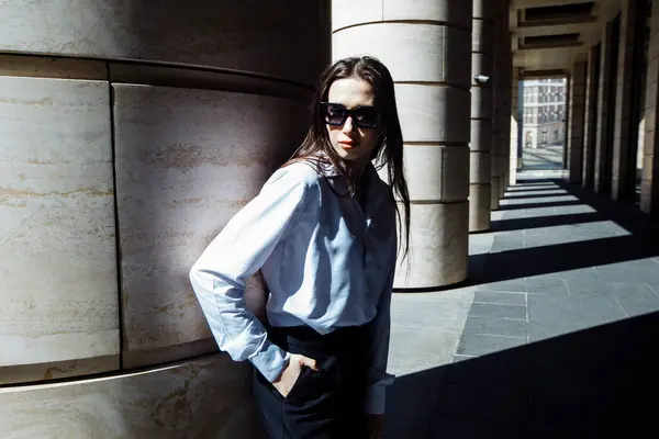 Sokakta poz veren uzun saçlı ve güneş gözlüklü kendine güvenen güzel bir kadının açık hava portresi..