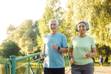 Sağlık, gülümseme ve spor, spor ve spor için parkta yaşlı bir çiftle koşmak. Sağlık, emeklilik ve motivasyon, spor ya da kardiyo eğitimi alan üst düzey erkek ve kadınların mutluluğu.