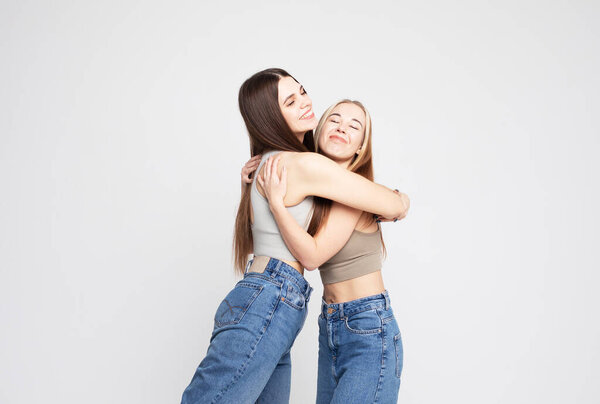 Studio shot of two happy young women friends isolated over white grey background