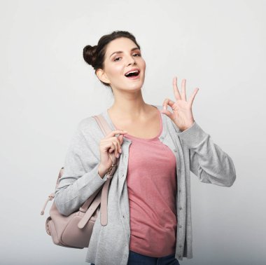 Yaşam tarzı, duygu ve gençlik kavramı: Sırt çantalı hoş bir genç kadın. Gri arkaplan üzerinde işaret var.