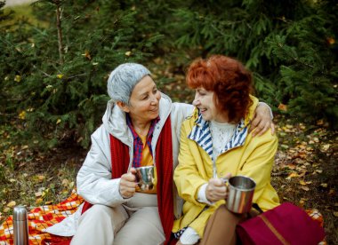 İki yaşlı kadın arkadaş ormanda yürüyor, termostan kahve döküyor, birlikte harika vakit geçiriyorlar. Yaşam tarzı ve insan kavramı.