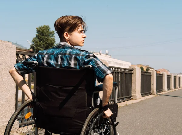 一个年轻的残疾人骑着轮椅过桥 年轻的男性穿着格子呢衬衫和牛仔裤 残疾人康复 保健和支助的概念 — 图库照片