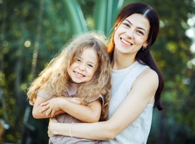 Happy summer time. Little daughter hugging her young happy mom in the park.