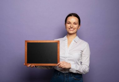 Young smiling woman holding a chalkboard isolated on purple background.
