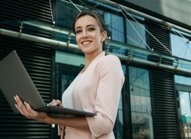 İş, iletişim, teknoloji ve insan konsepti - arka planda ofis binaları ile sokakta dizüstü bilgisayarı olan genç bir iş kadını