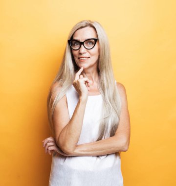 Yaşam tarzı, duygu ve yaşlılar konsepti: Sarı arkaplan üzerinde sarışın iyimser yaşlı kadının portresi