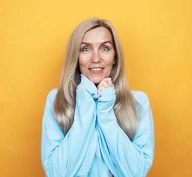 Güzellik, moda ve yaşlılar konsepti: uzun, güzel, gri saçlı, yaşlı bir kadın. Sarı arka planda şampuan ve sağlıklı saç konsepti.