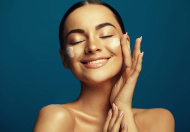 Yüz kremi süren güzel bir kadının güzel portresini kapat. Gözleri kapalı bir kadın manken. Mavi arkaplanda portre.