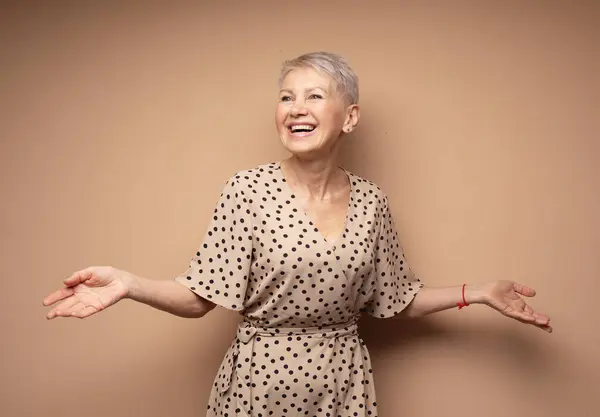 Beautiful elderly woman with a short pixie haircut in a polka dot dress. Delight and happiness.