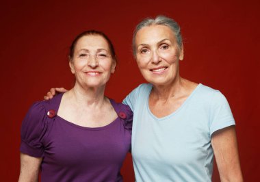 Kırmızı arka planda iki yaşlı ve güzel bayan arkadaş. Yaşam tarzı kavramı.