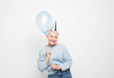 Güzel görünümlü, çekici, neşeli, neşeli, neşeli, gri saçlı, mavi balonlu kadının portresi beyaz gri arka planda izole edilmiş eğleniyor.