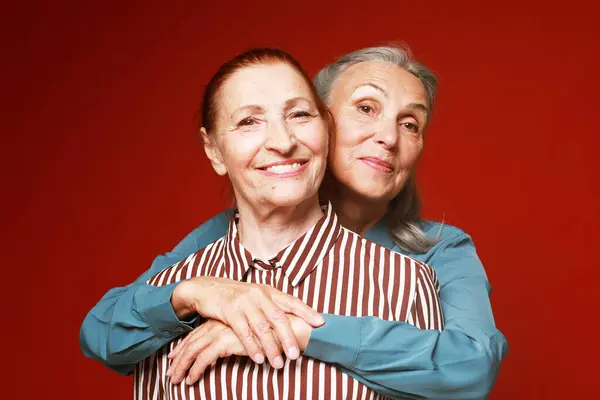 赤を背景に抱き合っている2人の年配の女性の友人 ライフスタイルと高齢者のコンセプト — ストック写真
