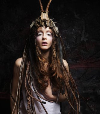 Parlak makyajlı, örgülü ve kafasında kafatası olan genç bir kadın karanlık arka plan partisinde, karnavalda, cadılar bayramında poz veriyor..