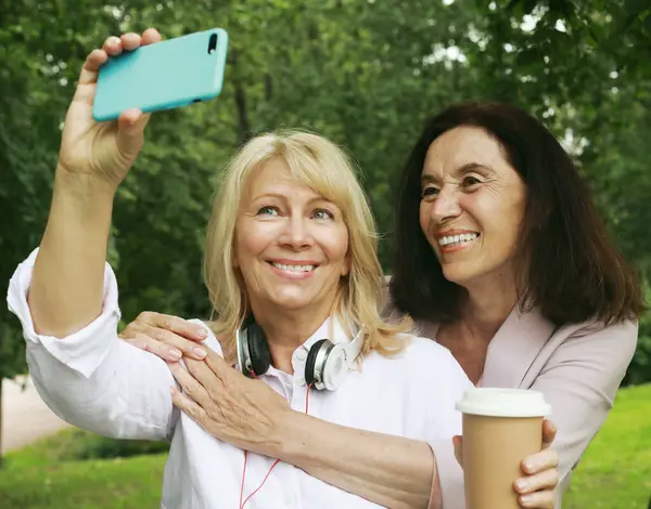 Two cheerful old women making selfie in summer park. Lifestyle concept.