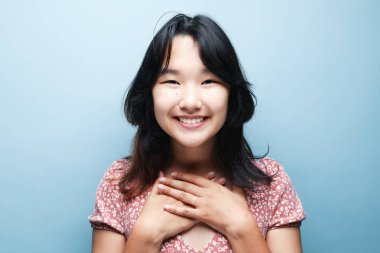 Samimi esmer kadın modelinin portresi mutluluğu geniş bir şekilde ifade eder. Beyaz dişler bile mavi arka planda izole edilmiş pembe elbiseler giyer.