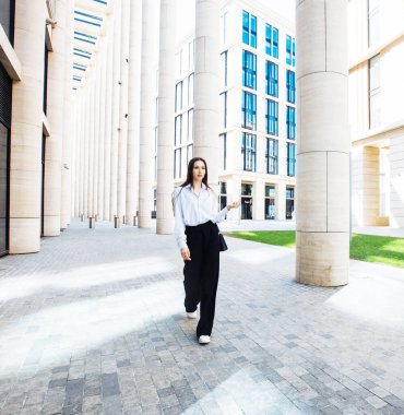 Siyah pantolonlu, beyaz pamuklu bluzlu, dışarıda poz veren şık bir kadın manken. Moda ve insanlar konsepti.