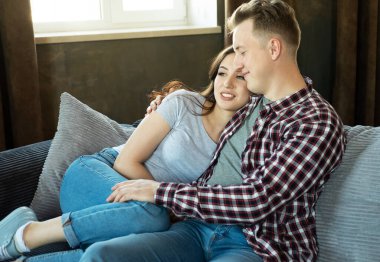 Genç ve güzel bir çift kanepede oturuyor ve sarılıyorlar. Yaşam tarzı ve insan kavramı.