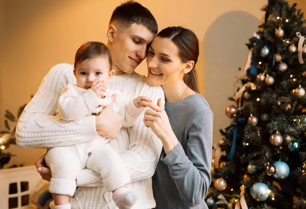 happy father standing near wife holding cute little baby daughter, christmas concept