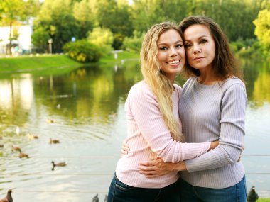İki kadın gölün yanında sarılıyor. Anne ve kızı, mutlu ve güzel. Parkta yaz günü.