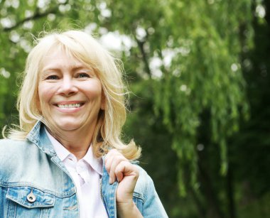 Beautiful blonde woman in a denim jacket in a spring park. Elderly happy lady pensioner. Close up. Golden age.