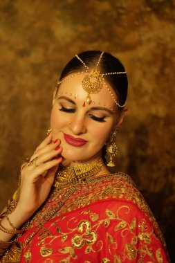 Lovely young woman wearing traditional indian red sari and jewelry, beauty smiles and looks down. Indian, Muslim, Arabic culture.