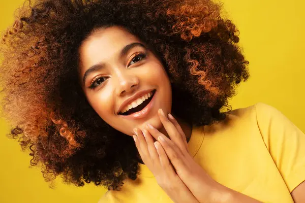 lifestyle, emotion and people concept: Surprised amazed beautiful afro woman with wide open mouth looking at camera, smiling. Girl posing on yellow background.