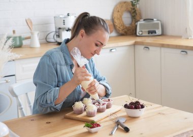 Yemek pişirme, Serbest Çalışmalar, İnsanlar ve Hobiler konsepti: Günlük dekorasyon giysileri giyen genç bir kadın beyaz kremalı kekleri süsledi.