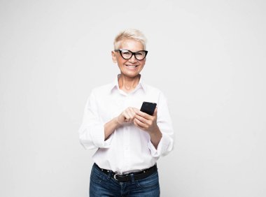 Güzel bir emekli kadın cep telefonu. Modern, son sınıf öğrencisi bir kadın elinde akıllı bir telefon tutuyor ve bir ürünü sunan telefonu gösteriyor..