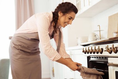 Genç gülümseyen kadın pasta şefi kek pişirmek için fırına koyar..