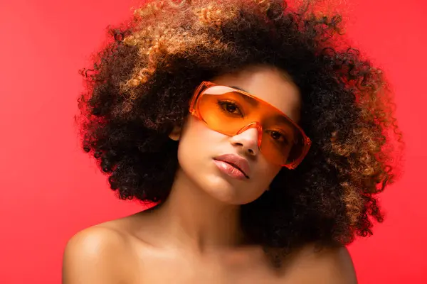 Happy Afro woman wearing eyeglasses smiling, has good mood isolated on studio red background.