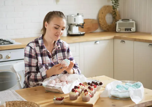 Young smiling woman pastry chef decorates marshmallows. Food concept.