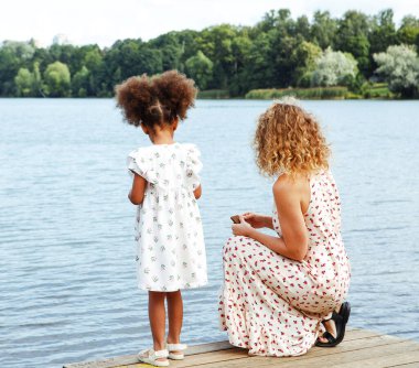 Genç beyaz bir anne ve büyüleyici esmer tenli bir kız suya bakar, kuşları küçük bir platformdan, yaşam tarzından ve insanların konseptinden izler..