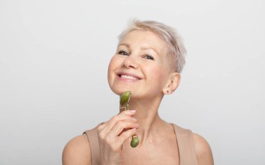 Güzel bir yüz portresi. Kısa saçlı, tatlı ve son sınıf öğrencisi bir kadın. Yüz masajını mükemmel bir cilt için kullanıyor.