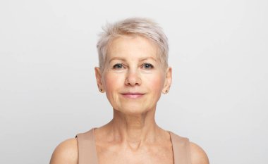 Açık gri arka planda kısa saçlı olgun bir kadının güzel portresi.