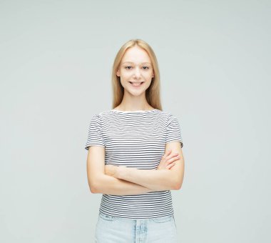 Açık gri arka planda çapraz kollu çizgili tişört giyen güzel, gülümseyen sarışın kadın..