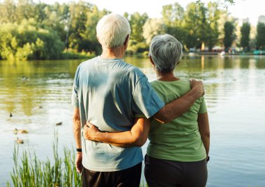 Gölün kenarında emekli bir çift yaz günü gün batımına hayran kalır. Arkadan bak. Altın çağ. Sevgi ve şefkat.