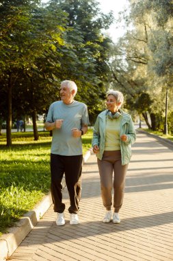 Yaşlı bir çift parkta birlikte koşuyor. Zayıflama egzersizleri yaparken birbirlerine bakıyorlar. Yaşam tarzı, insanlar ve spor anlayışı.