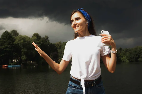 Young woman listens to music and enjoys vacation, weather before thunderstorm, lake, summer. Lifestyle and people concept.