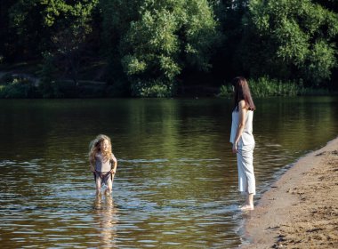 Beş yaşındaki neşeli bir kızın ve annesinin göl kenarında çıplak ayakla yürüdüğünü, yaz günü eğlendiklerini görüyorum. Mutlu yaz zamanları..