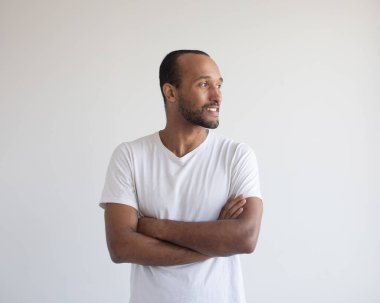 Açık gri arka planda kolları çapraz duran yakışıklı Afro-Amerikan bir adamın portresi.