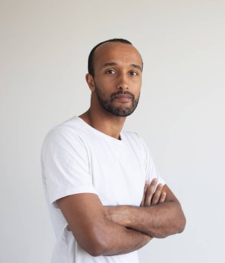 Açık gri arka planda kolları çapraz duran yakışıklı Afro-Amerikan bir adamın portresi.